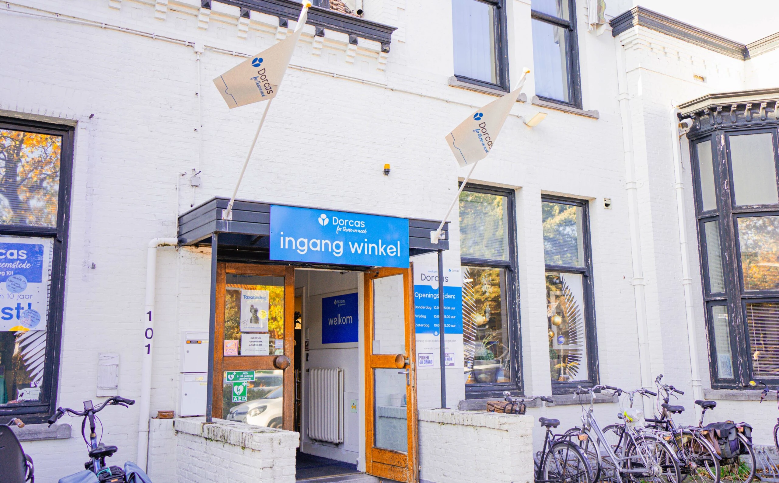 Ingang van de Dorcas winkel in Heemstede met blauwe winkelborden en fietsen voor de deur, klaar voor bezoekers die goede tweedehands spullen willen kopen of doneren.