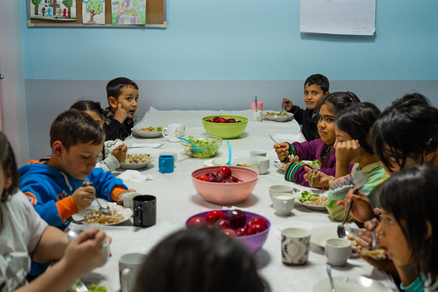 Kinderen eten pasta aan een grote tafel 