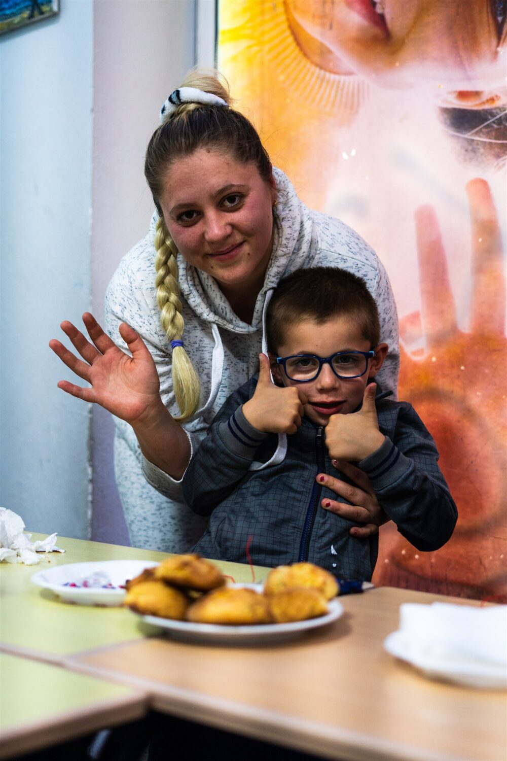 Kozeta en haar zoon zwaaien naar de camera en steken hun duim op