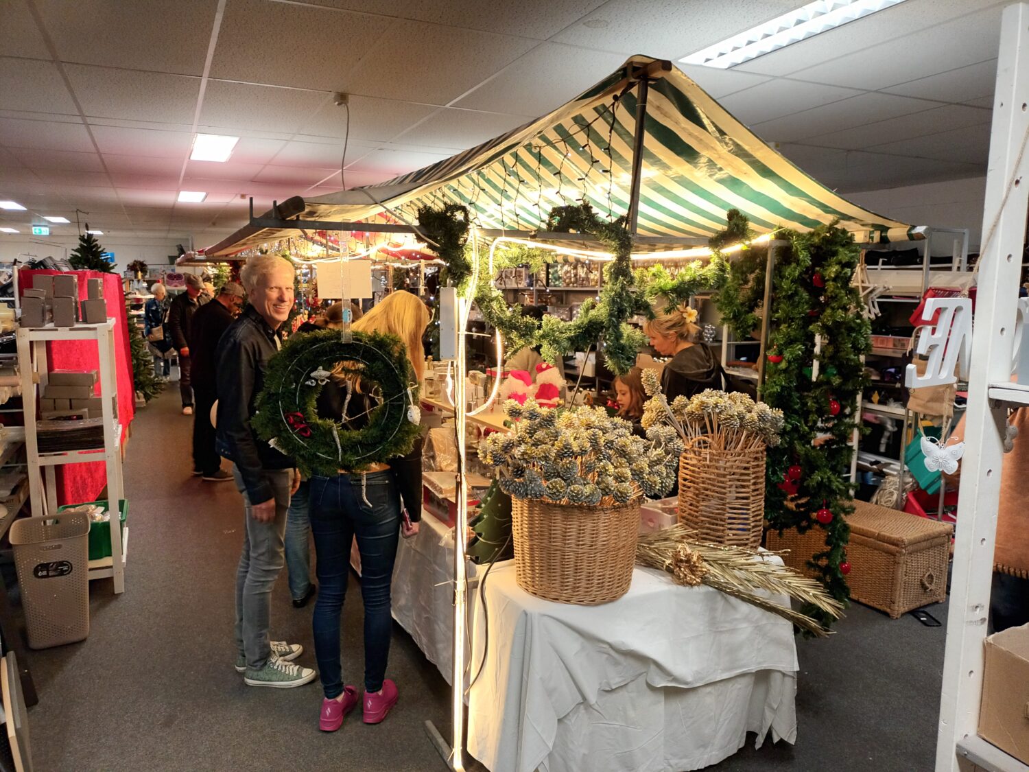 Decoratieve kerstmarktstand met kerstversieringen en bloemen bij Dorcas in een winkelcentrum.