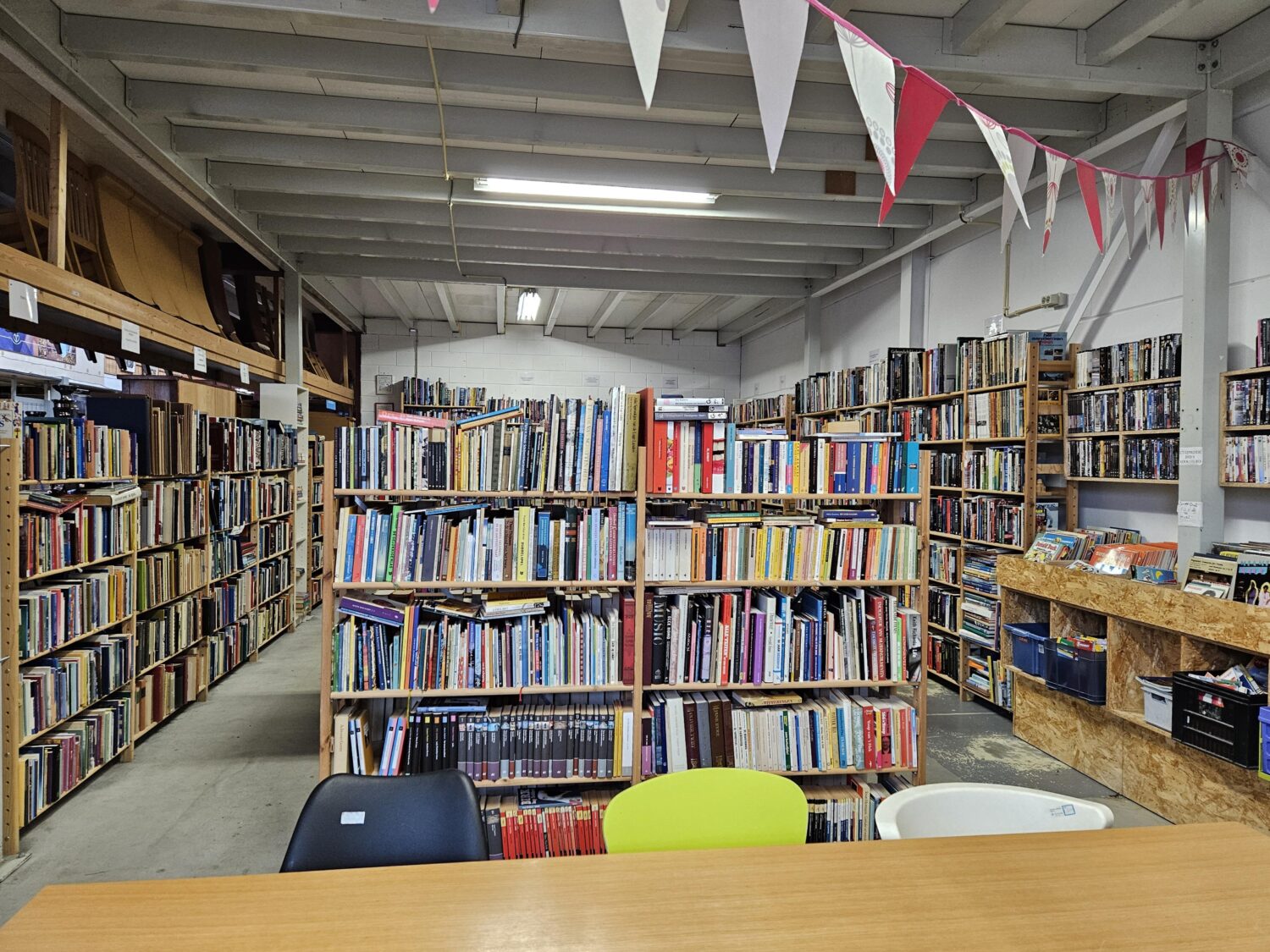 Veel boeken in een tweedehandsboekwinkel met houten rekken en kleurrijke kaften, klaar om te worden gelezen of verkocht.