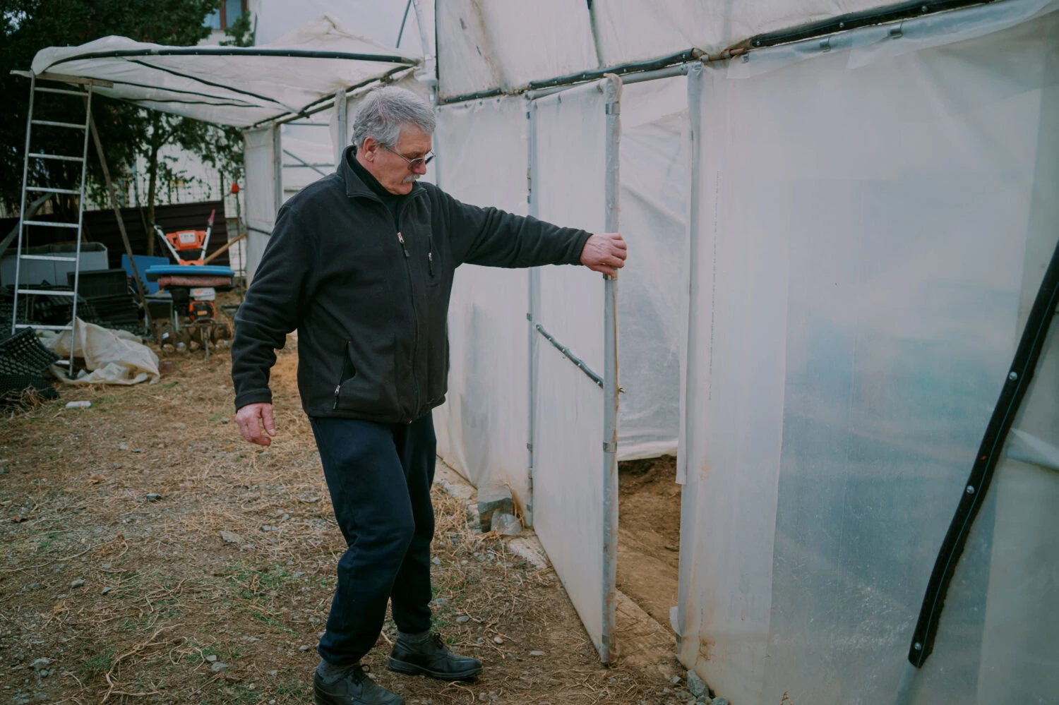 Een man opent een deur van een kas of serre, buiten in een tuin of op een landbouwbedrijf, betrokken bij tuinbouw of landbouwactiviteiten.