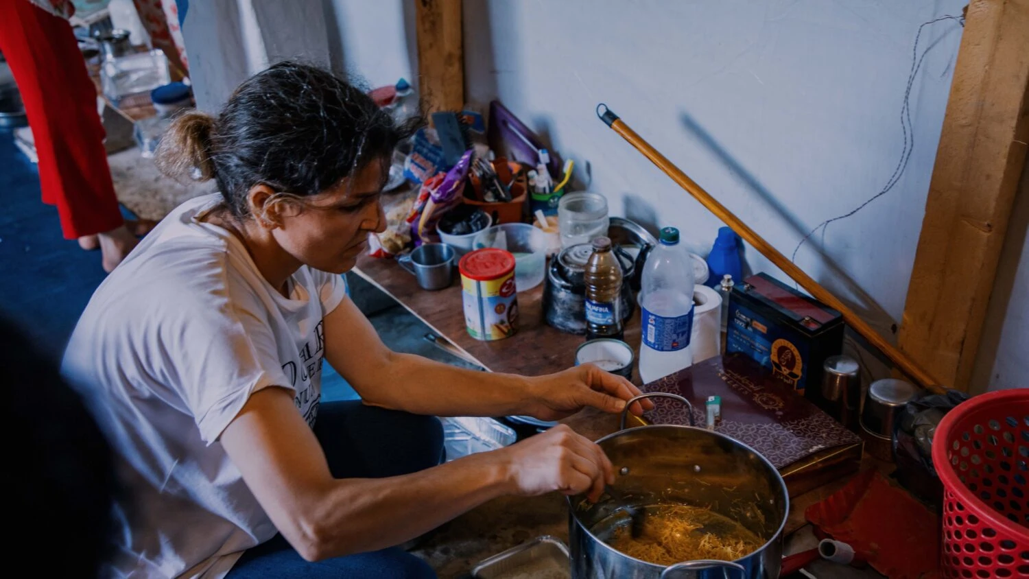 Gezouten vrouw die samen een warme maaltijd bereidt in een eenvoudige keuken met diverse ingrediënten en keukengerei.