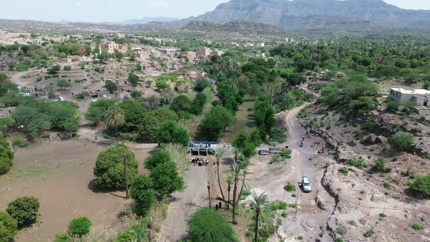 Gezicht op een dorpsgebied in een bergachtig landschap met groene bomen en eenvoudige huisjes, omlijst door bergen en heuvels