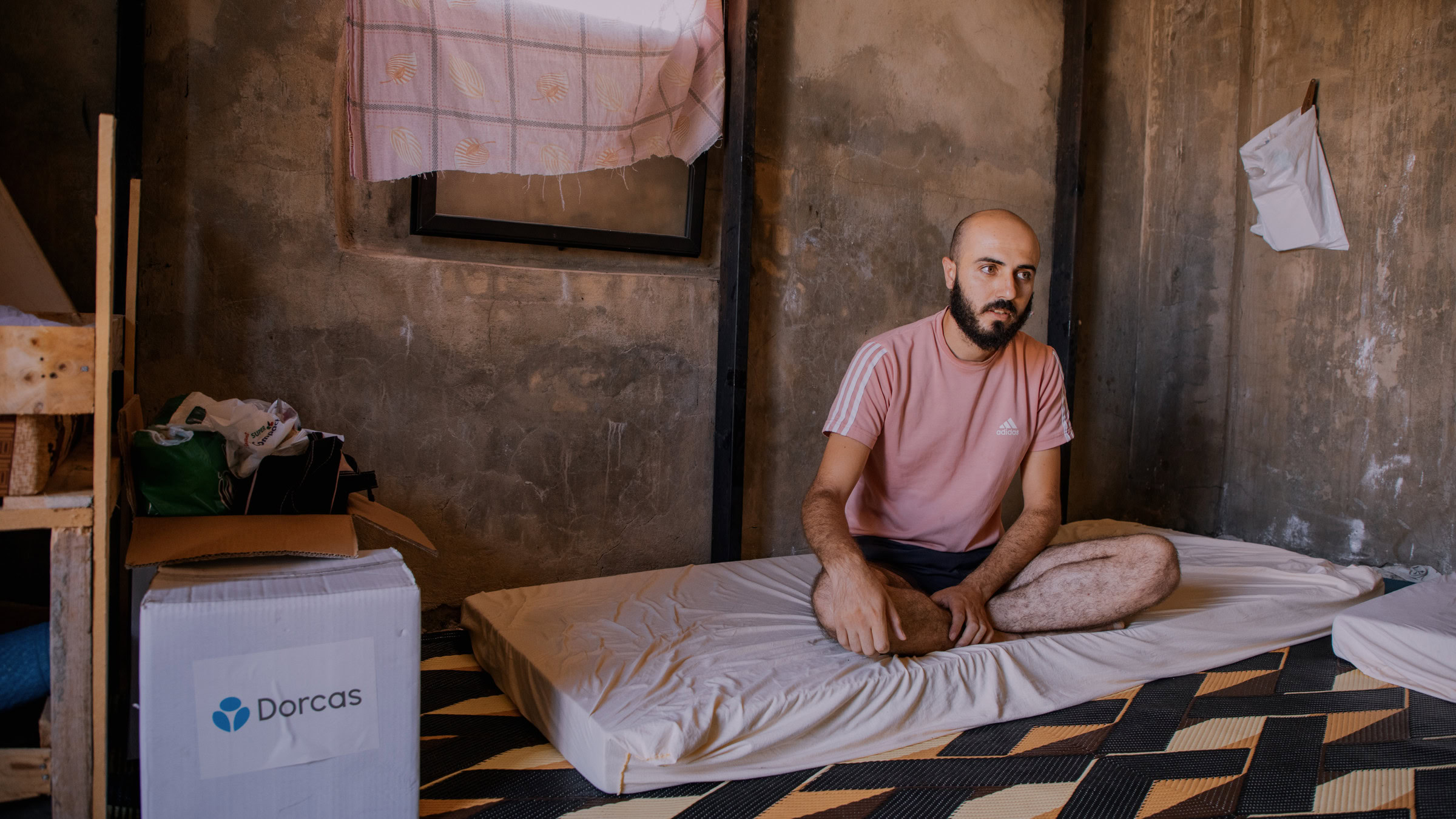 Minimalistisch geïnrichten kamer met een man die op een matras zit, duurzaam en sociaal bedrijfsmodel van Dorcas zichtbaar op de doos.