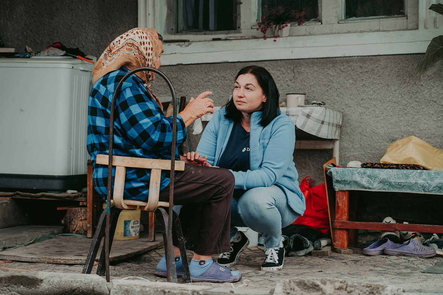 Zorgvrijwilliger praat met oudere vrouw op trap voor huis, maatschappelijke hulp, betrokkenheid ouderen, vrijwilligerswerk bij Dorcas, lokale ondersteuning, Nederlandse gemeenschapszorg.