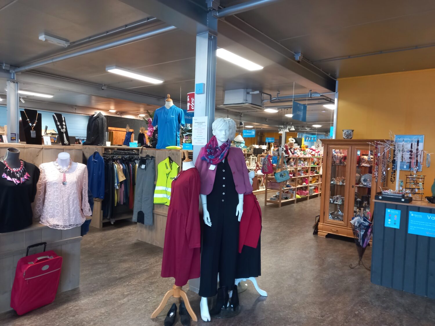 Diverse kleding en accessoires uit de winkel van Dorcas, met jurken, shirts en sieraden op mannequins en kledingrekken.