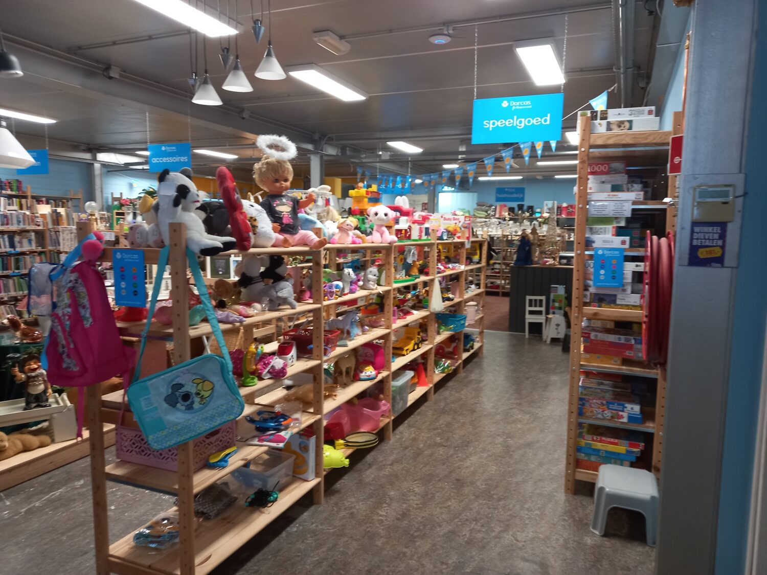 Leuk ingericht speelgoed afdeling in een Dorcas winkel met diverse knuffels, speelgoed en kinderaccessoires op houten rekken.
