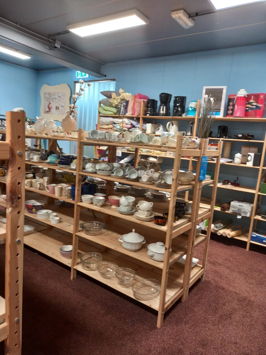 Diverse servies en keukengerei op houten winkelrekken in een tweedehandswinkel.