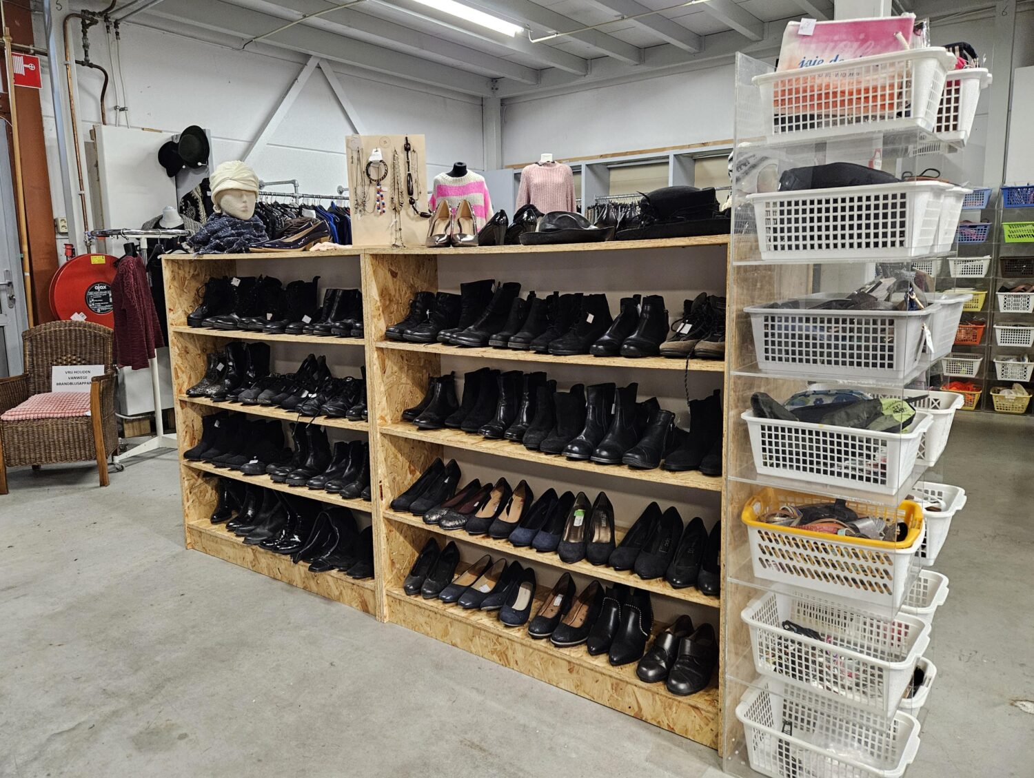 Dames schoenen en accessoires aan een houten winkelrek in een donatiewinkel van Dorcas, met diverse schoenen, tassen en kledingstukken.