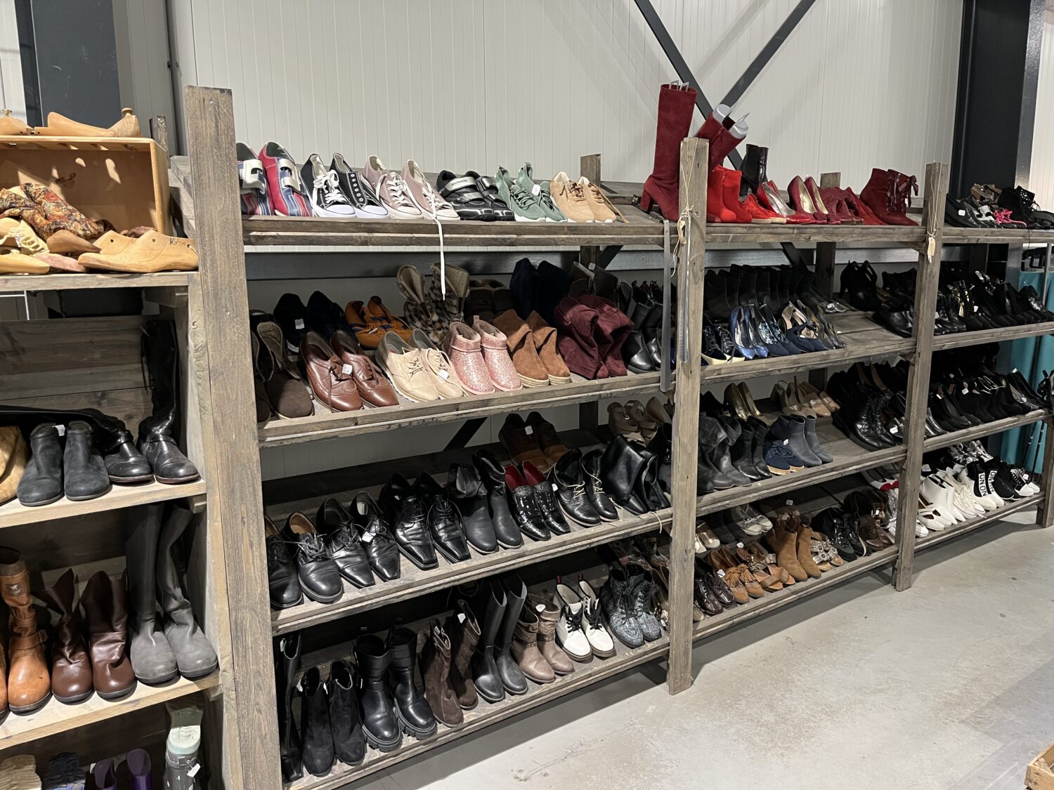 Diverse schoenen en laarzen op houten schoenenrek bij Dorcas; ruime selectie voor dames, heren en kinderen in verschillende stijlen en kleuren.