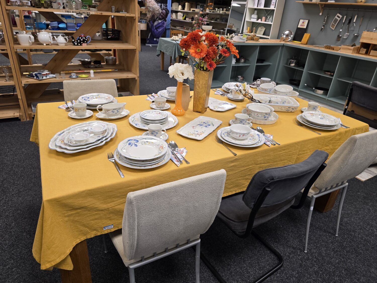 Elegante eettafelsetting met servies, kopjes en bestek, versierd met kleurrijke bloemen in vazen, geschikt voor dining experiences bij Dorcas winkel.