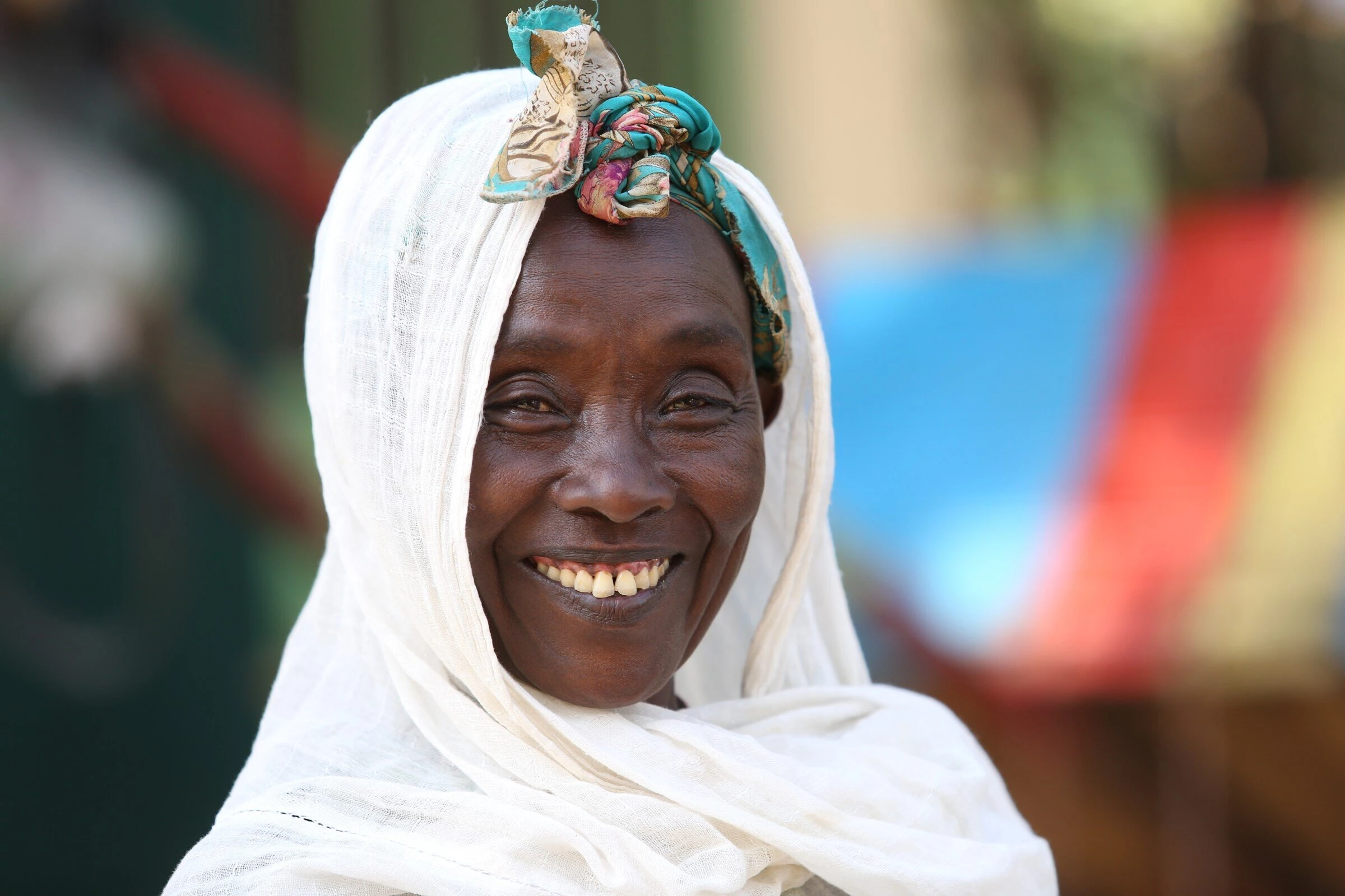 Lachende vrouw uit Afrika met witte hoofddoek en kleurrijke hoofdband, portret met lach en warmte, menselijke connectie, uitdrukking van vreugde en cultuur, dorcas.nl ondersteuning.