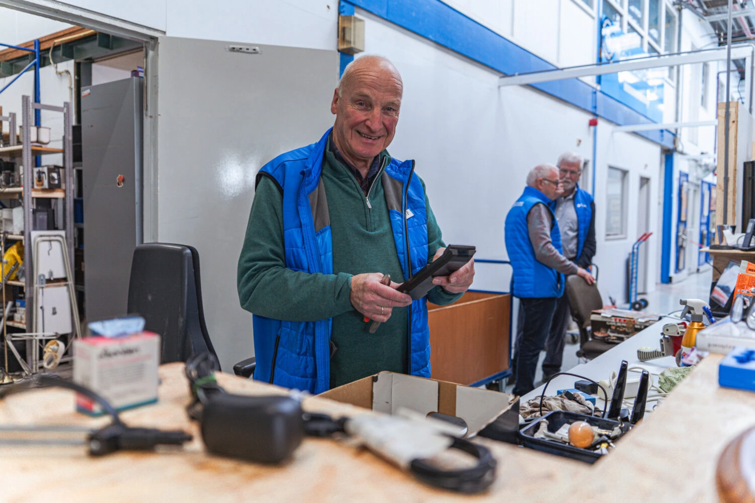 Mannelijke medewerker van Dorcas met tablet in grote werkplaats, bijdrage aan sociale initiatieven en recyclingprojecten.
