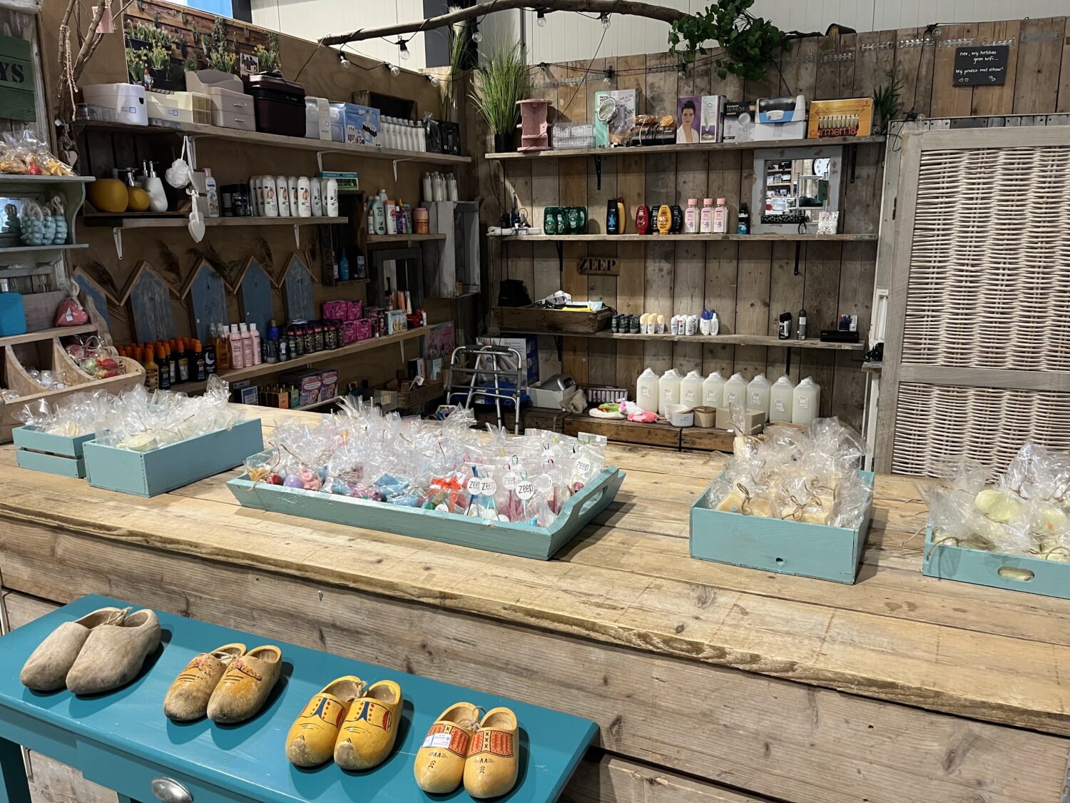 Grote houten tafel met handgemaakte souvenirs en cadeaus bij Dorcas winkel, sfeervolle inrichting met diverse verzorgingsproducten en knuffels op achtergrond.