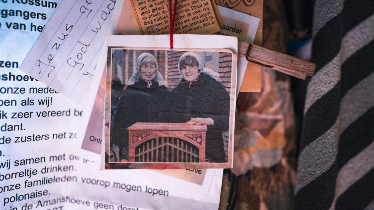 Twee vrouwen in gewaad poseren achter een houten object bij een herdenkings- of gedenkplek.