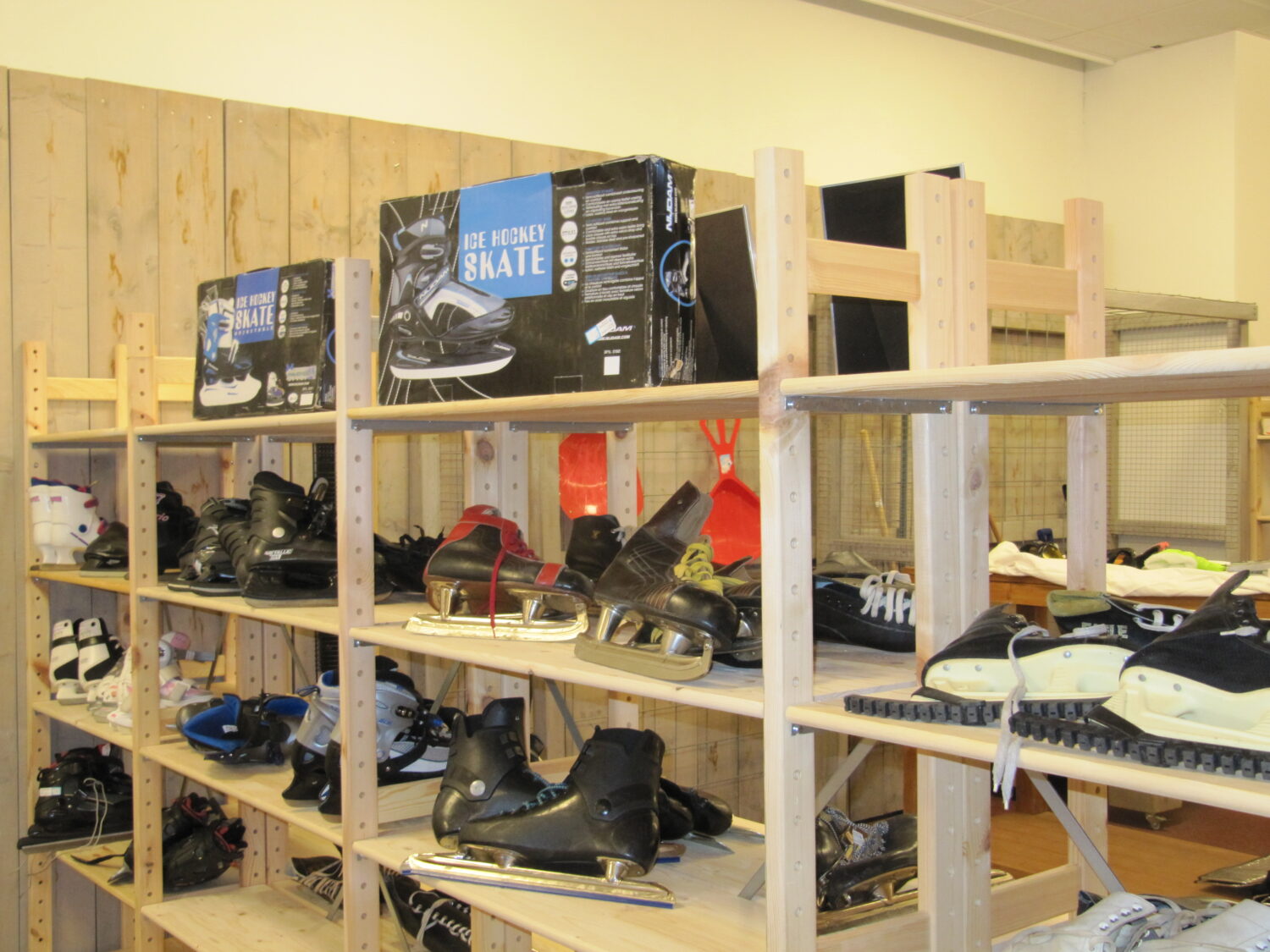Diverse ijshockeyschaatsen en skates op houten rekken in een sportwinkel of opslagruimte.