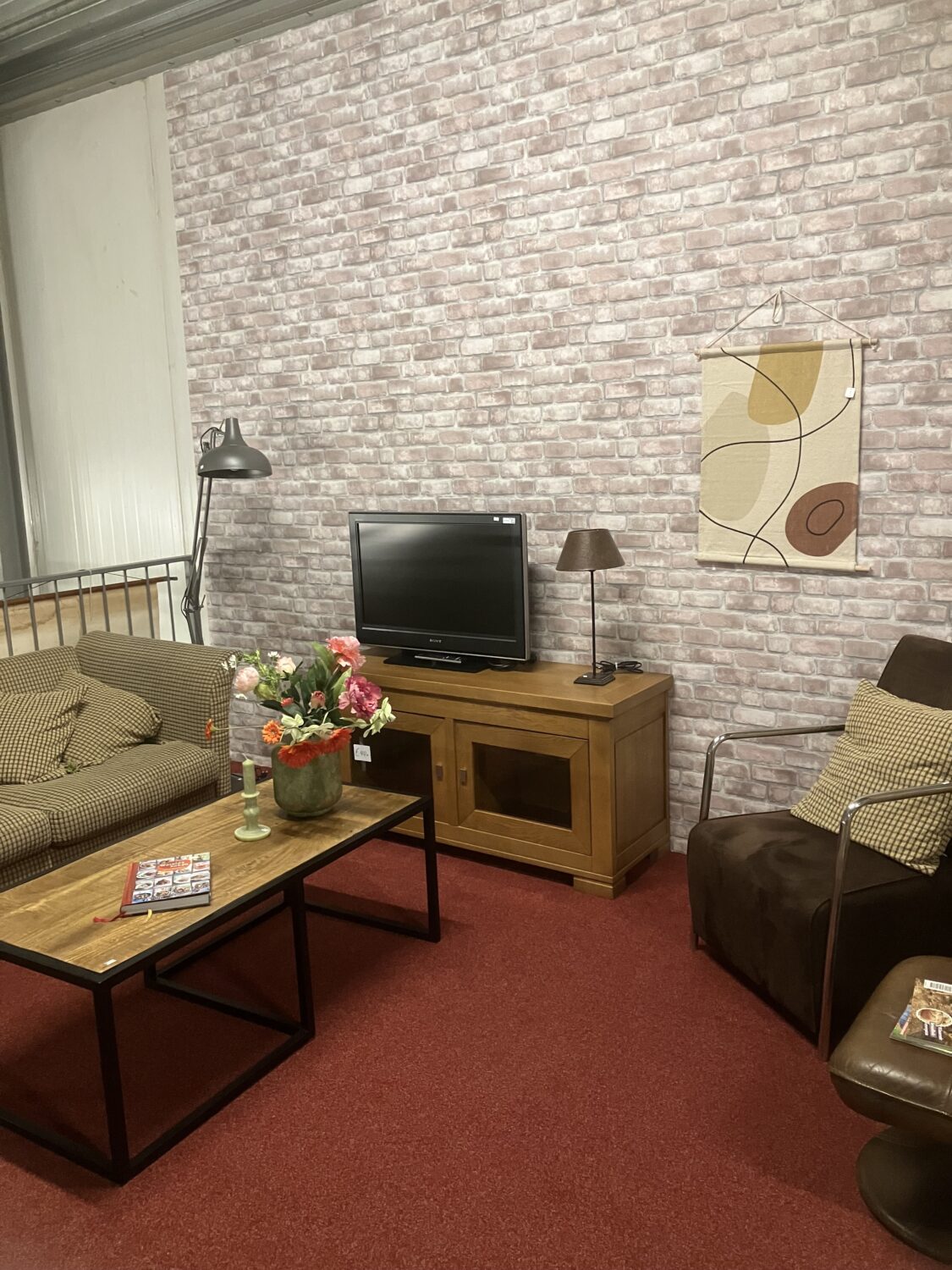 Gezellige woonkamer met vintage meubels, bloemenarrangement en een tv, ideaal voor ontspanning en samenkomen.