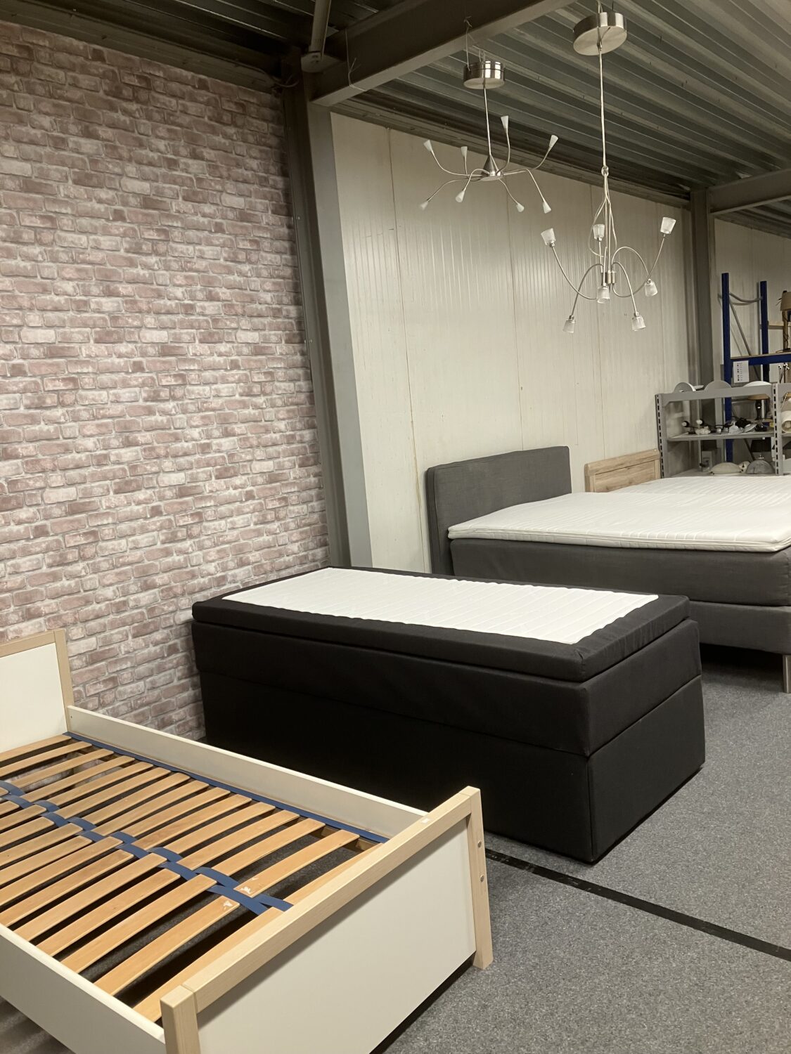 Diverse bedden en matrassen in een meubelzaak of showroom, inclusief een houten bedframe zonder matras, die klaar is voor verkoop of presentatie.