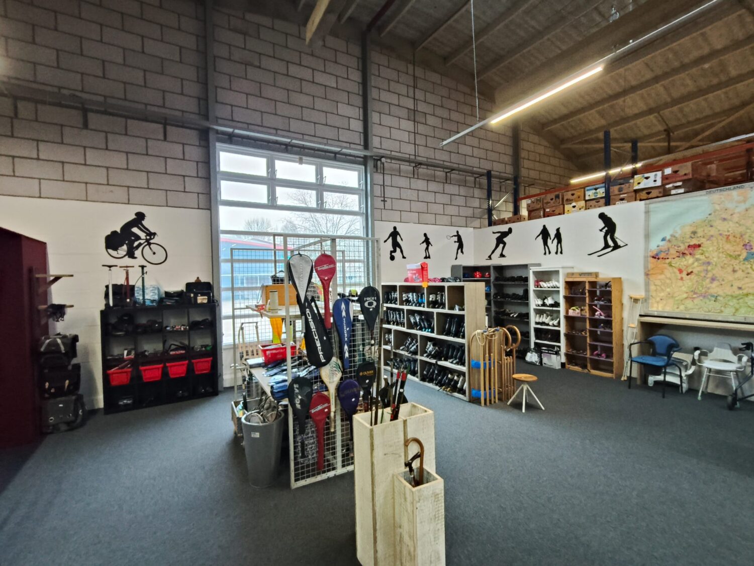 Interieur van een sportwinkel met skispullen, helmen, skischoenen en accessoires, gevestigd in een industriële ruimte met bakstenen muren en grote ramen.
