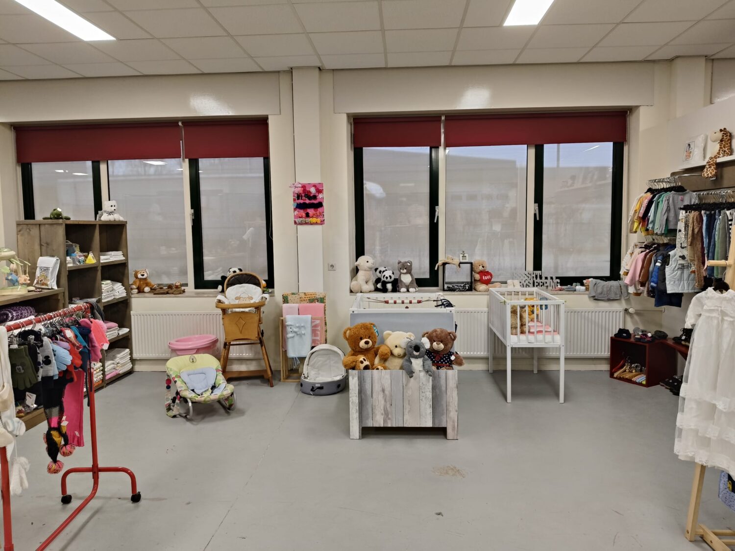 Een overzicht van een winkelruimte met kleding, speelgoed en accessoires voor goede doelen, ingericht met grote ramen, planken en displays voor donaties en verkoop.