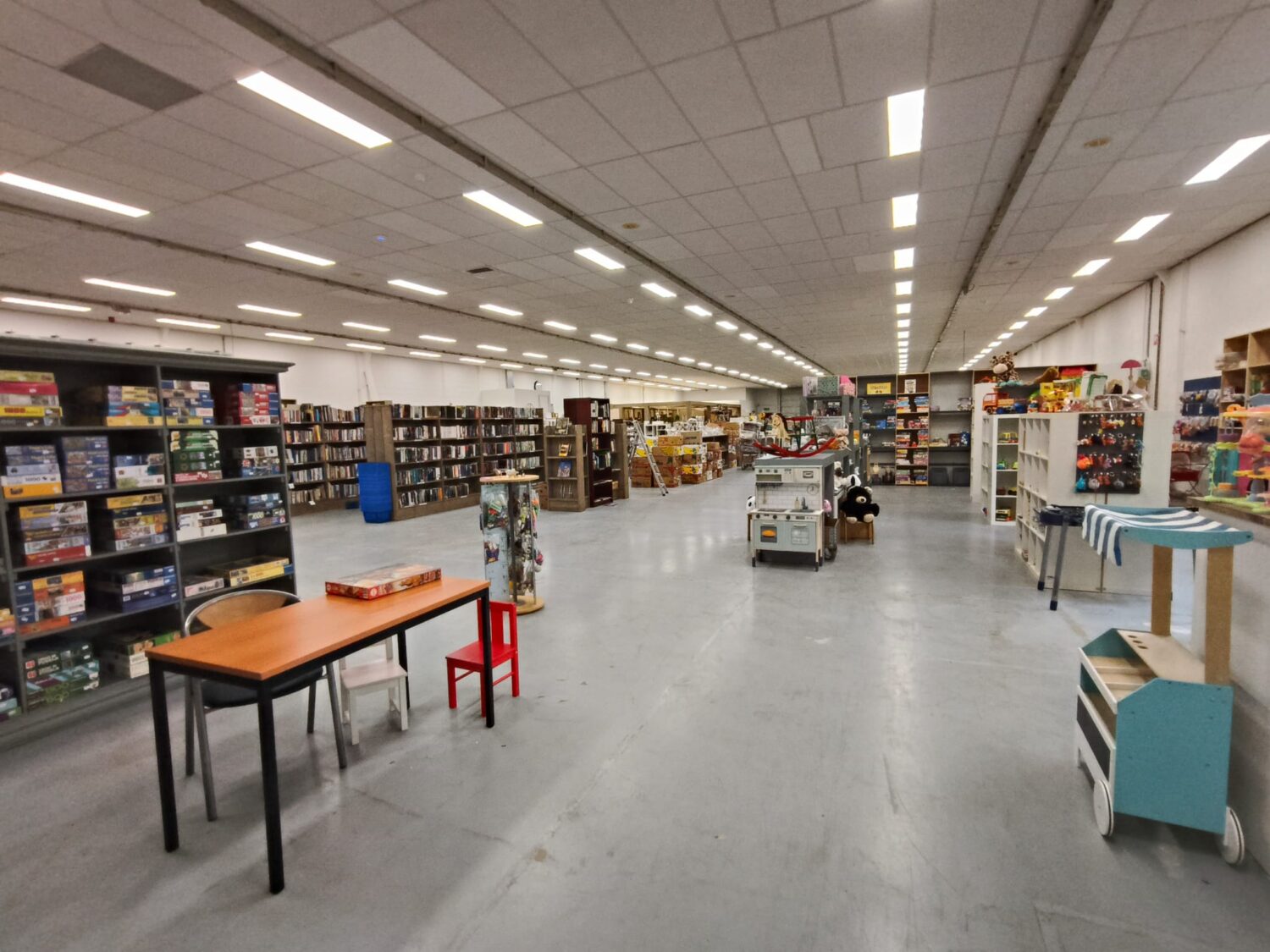 Klusruimte met lege schappen en tafels in winkel of magazijn, klaar voor nieuwe voorraad of inrichting, overzichtelijke en ruime opstelling voor efficiënt werken.