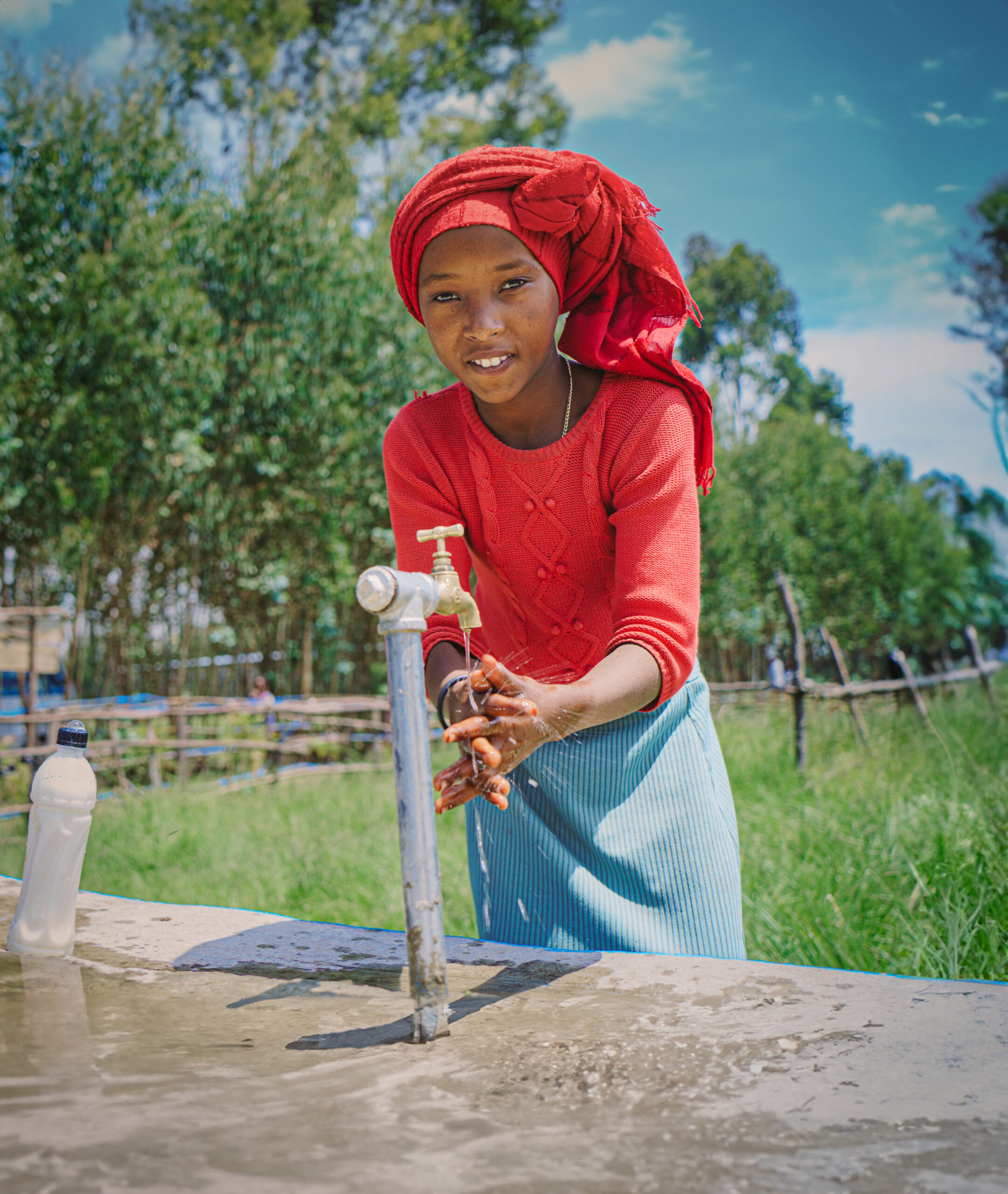 Vrouw wast haar handen bij een waterkraan in een landelijke omgeving, symboliseert toegang tot schoon water en hygiëne in ontwikkelingslanden.