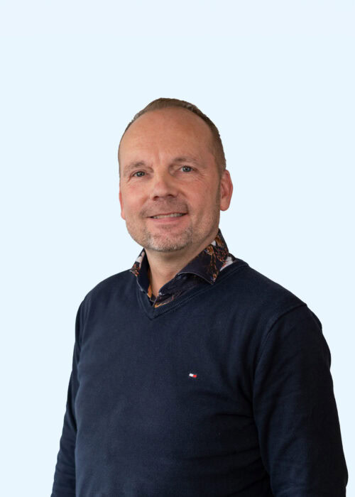 Een man glimlachend in een donkerblauwe trui, klaar om te helpen bij contactvragen op de website van Dorcas.