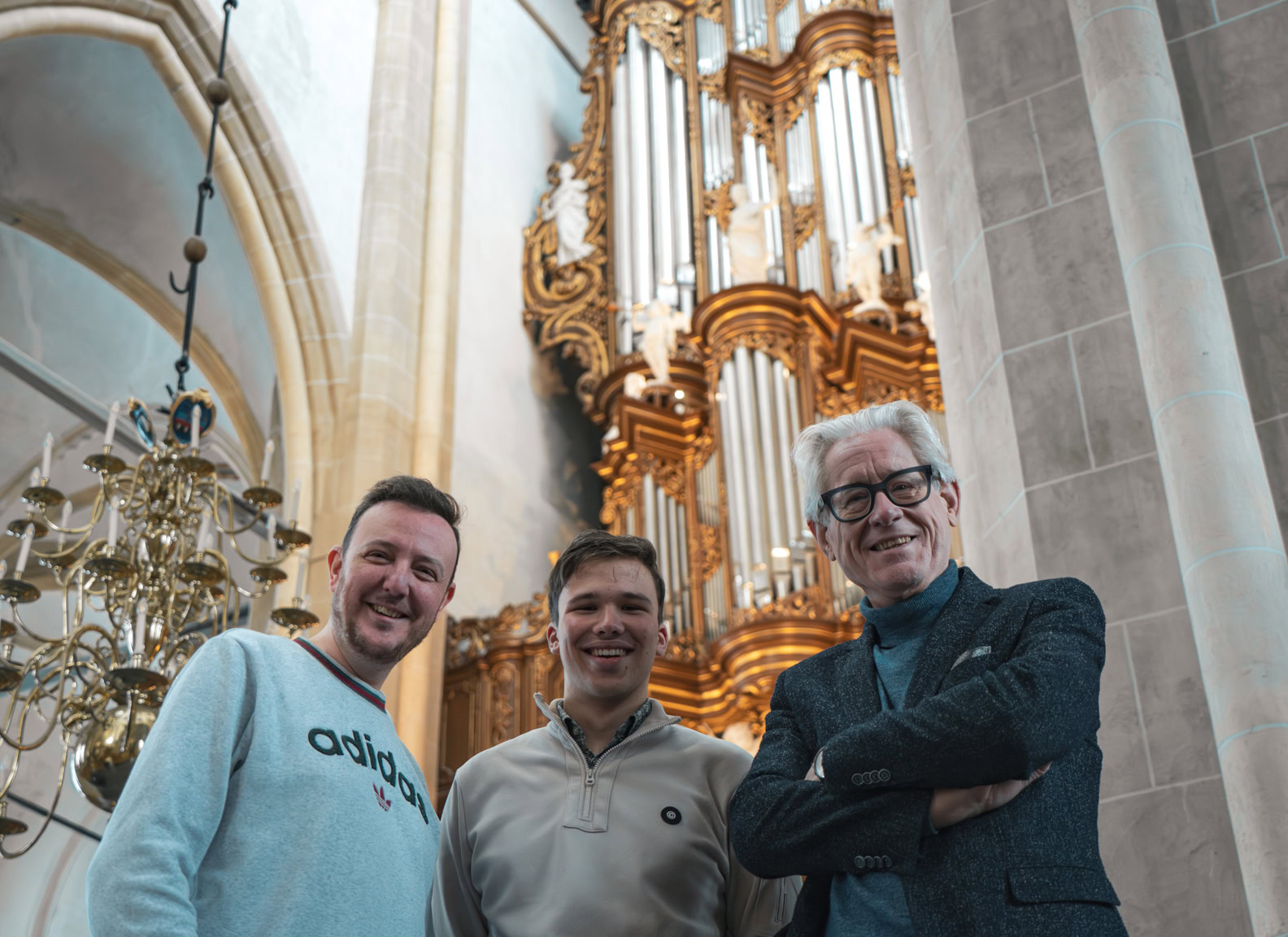 Een foto van drie mannen die in een kerk staan voor een groot orgel, lachend en in een ontspannen sfeer, tijdens het evenement Psalmenmarathon.