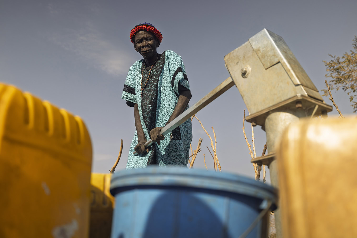 Een vrouw in traditionele kleding met waterpomp in een droge, dorre omgeving, symboliseert watertekort en de impact op gemeenschappen.