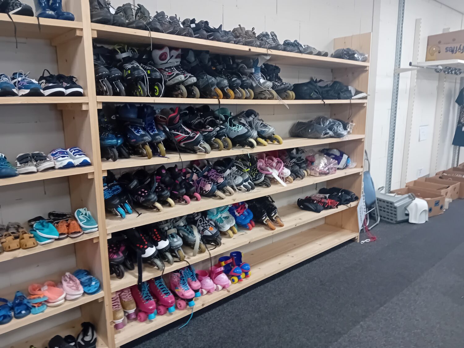 Een houten schoenenrek gevuld met diverse kinderschoenen, waaronder sneakers, laarzen en sandalen, in een winkel of opslagruimte.