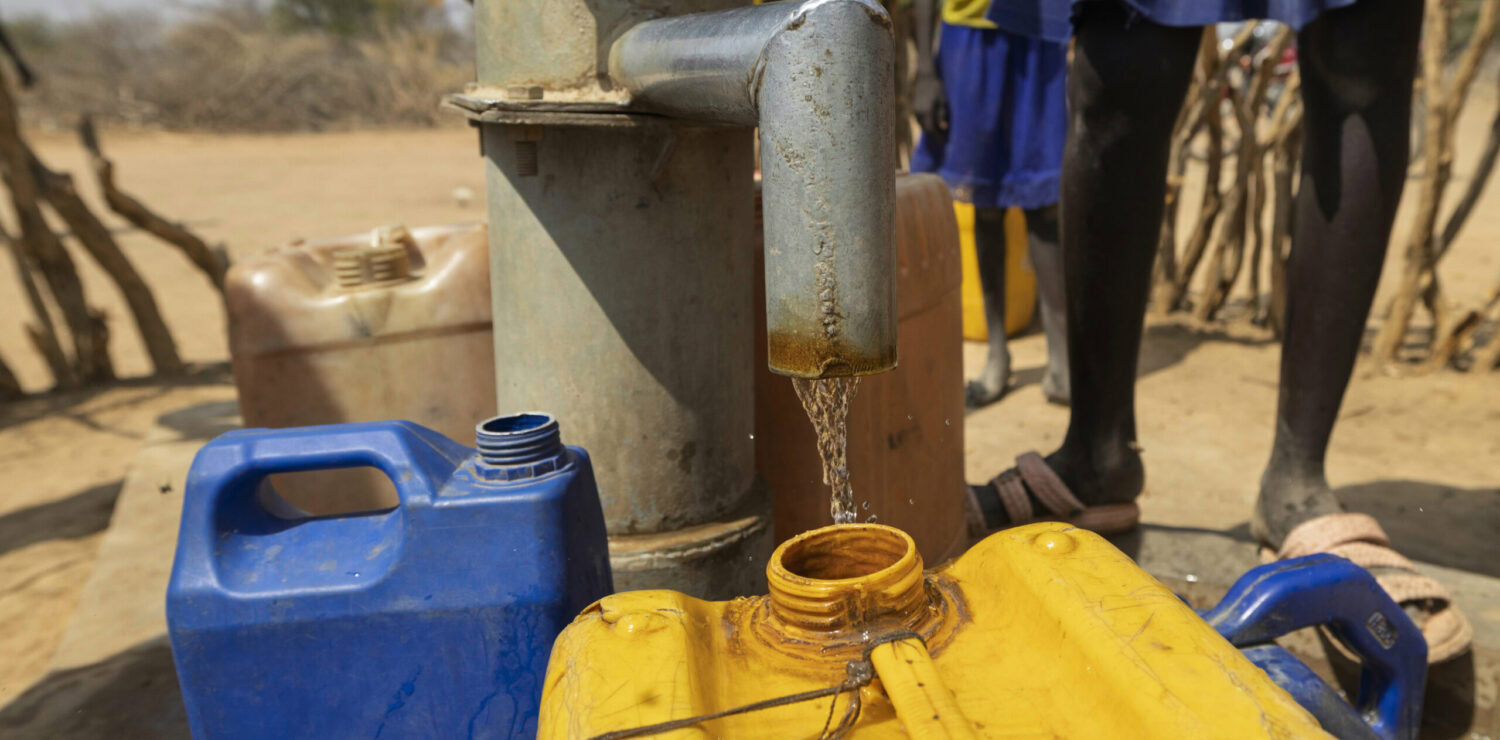Waterput met stromend water en jerrycans in een droge, landelijke omgeving.