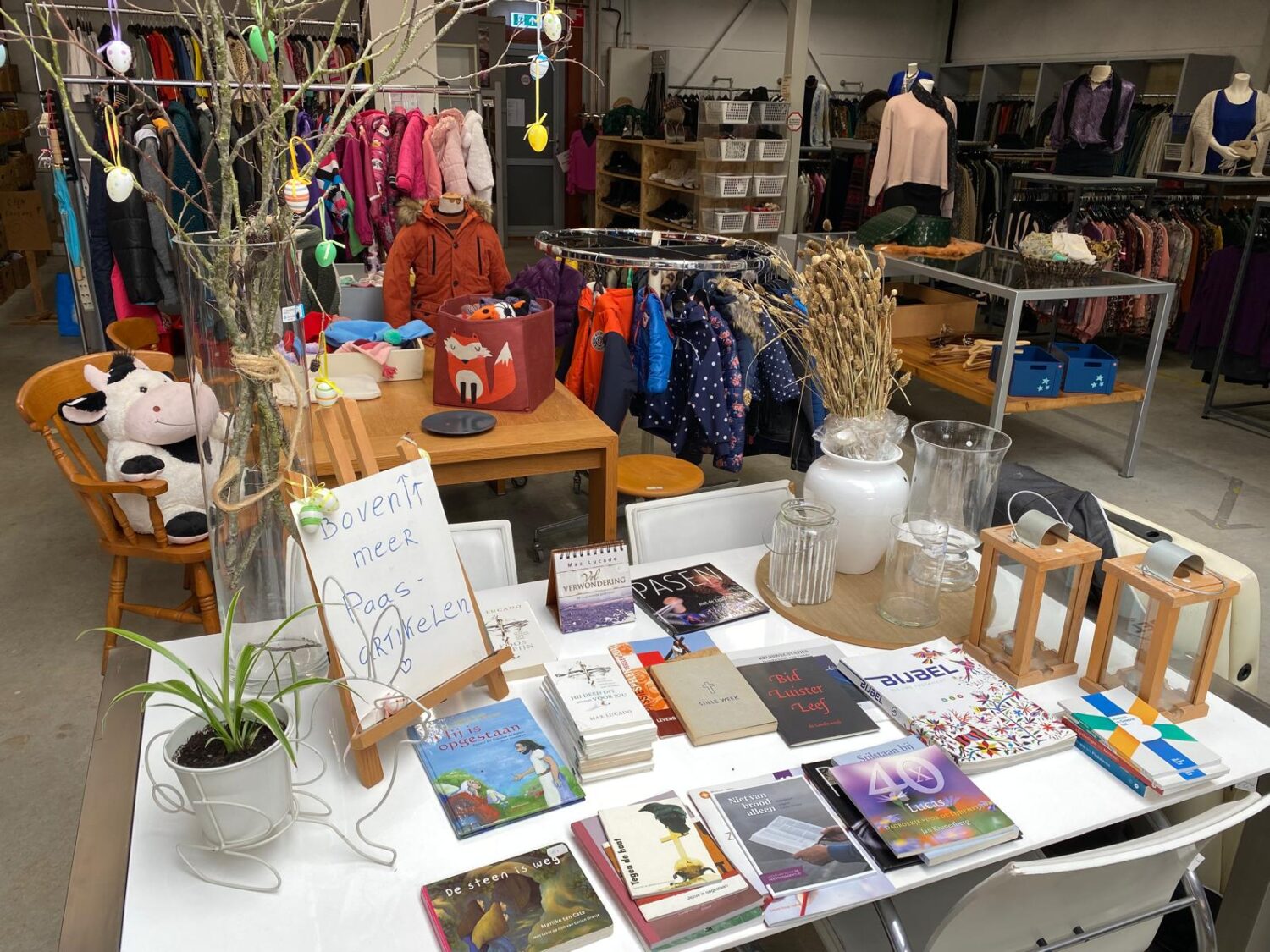 Een verkoopstand met tweedehands kleding, boeken en decoratieve items in een winkel of marktomgeving.