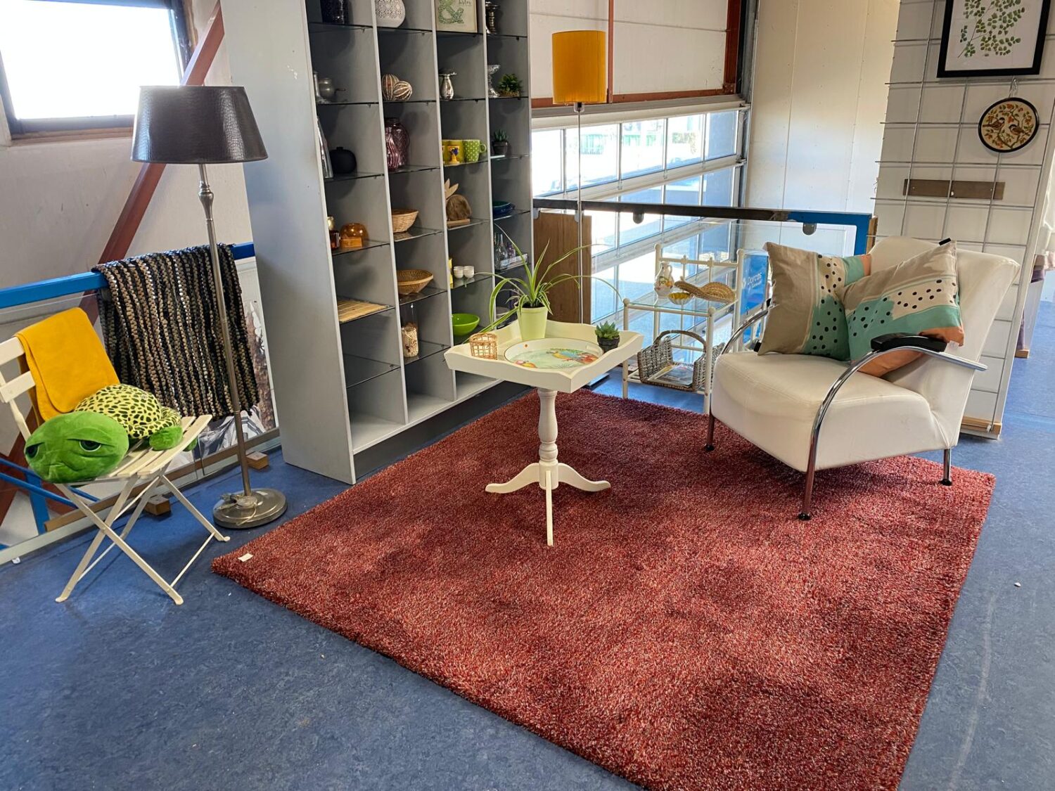 Een gezellige woonkamer met een comfortabele bank, een salontafel, en decoratieve kussens, ingericht met een kleurrijk tapijt en diverse woonaccessoires voor een warme sfeer.