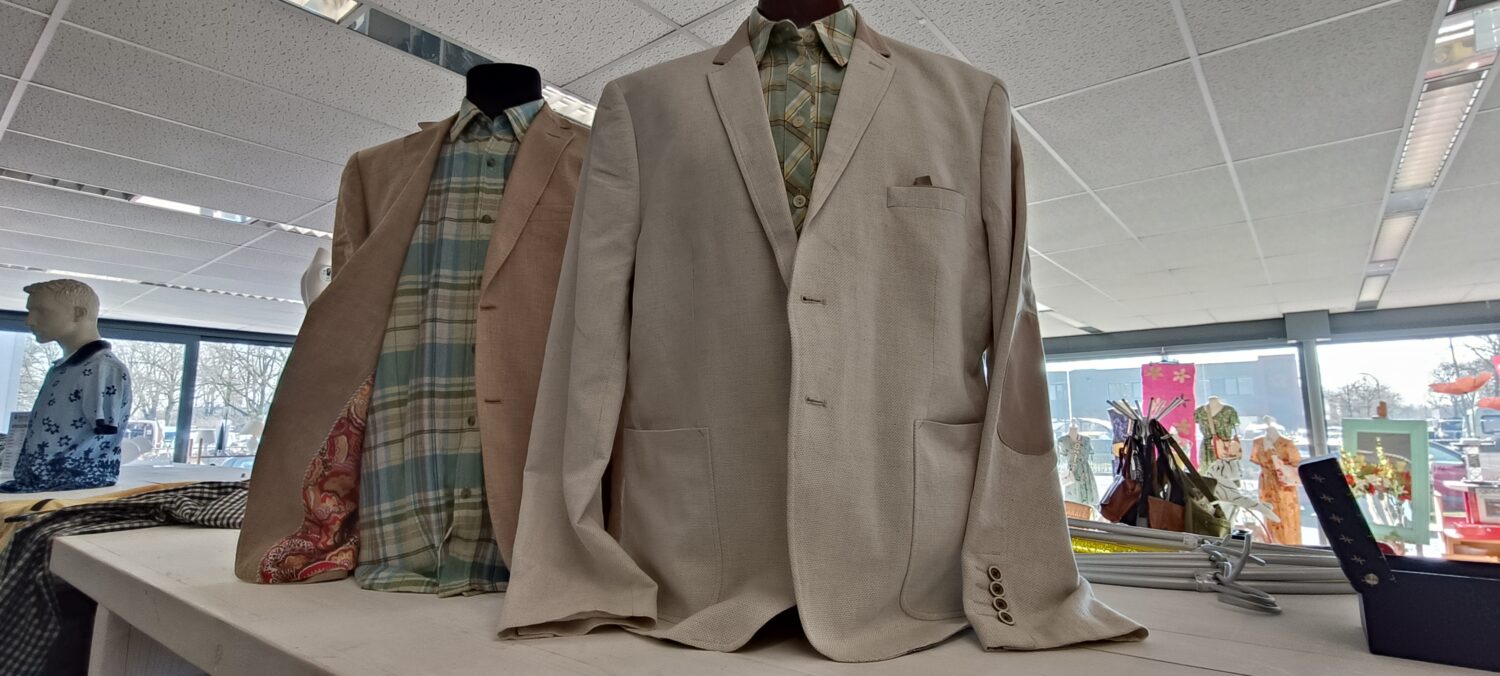 Mannequin met beige herensuit en overhemden in winkelruimte.