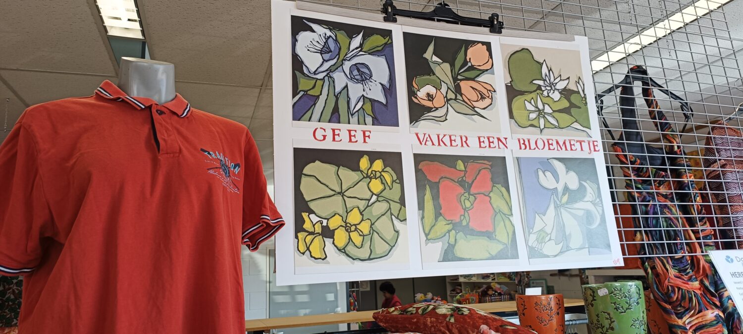 Een display met kleurrijke bloemkunst en een rood polo shirt in een winkelomgeving.