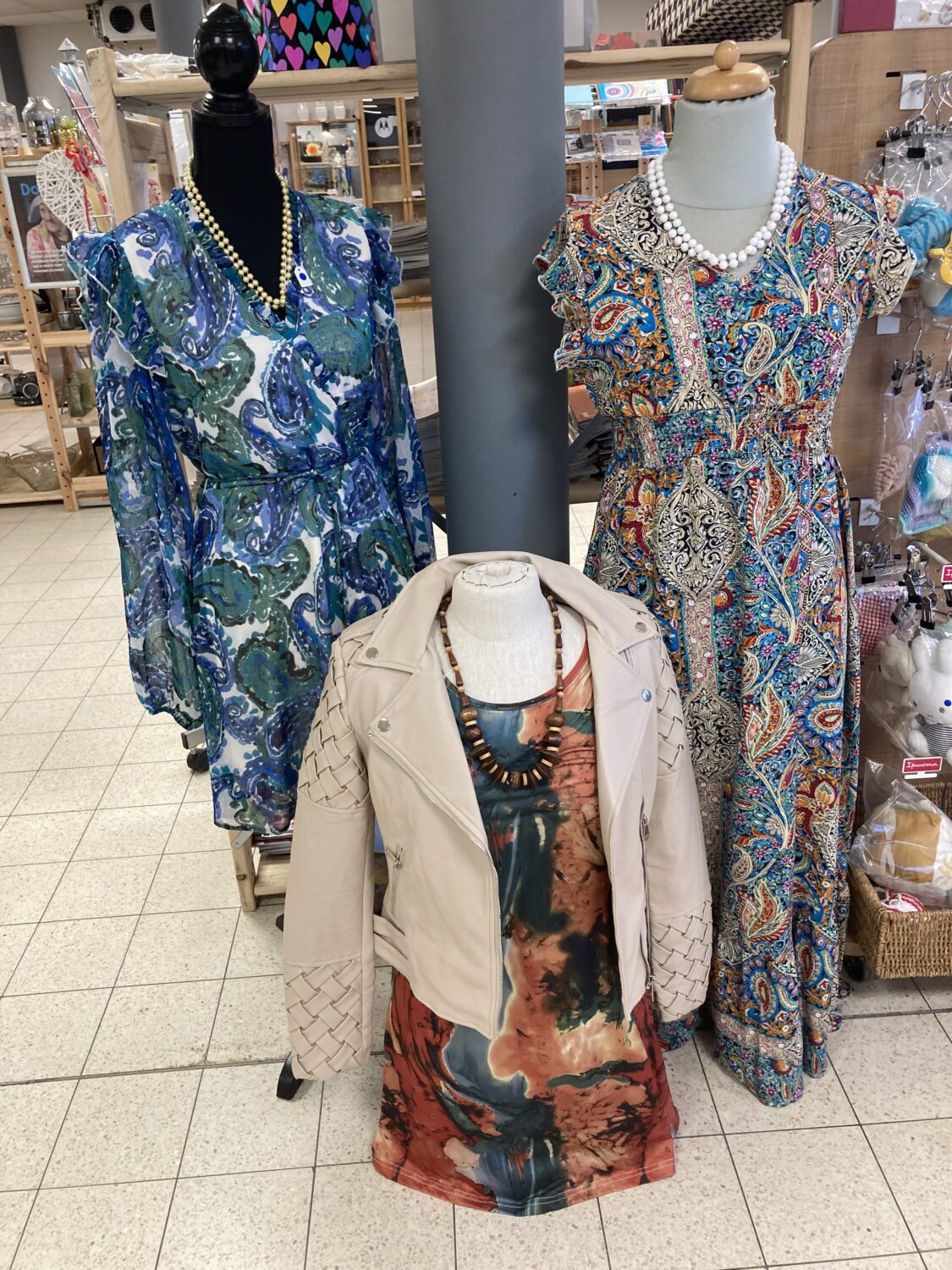 Een vintage damesjurk met een levendig, kleurrijk patroon, gecombineerd met een beige leren jas en bijpassende sieraden, perfect voor een stijlvolle en unieke look.