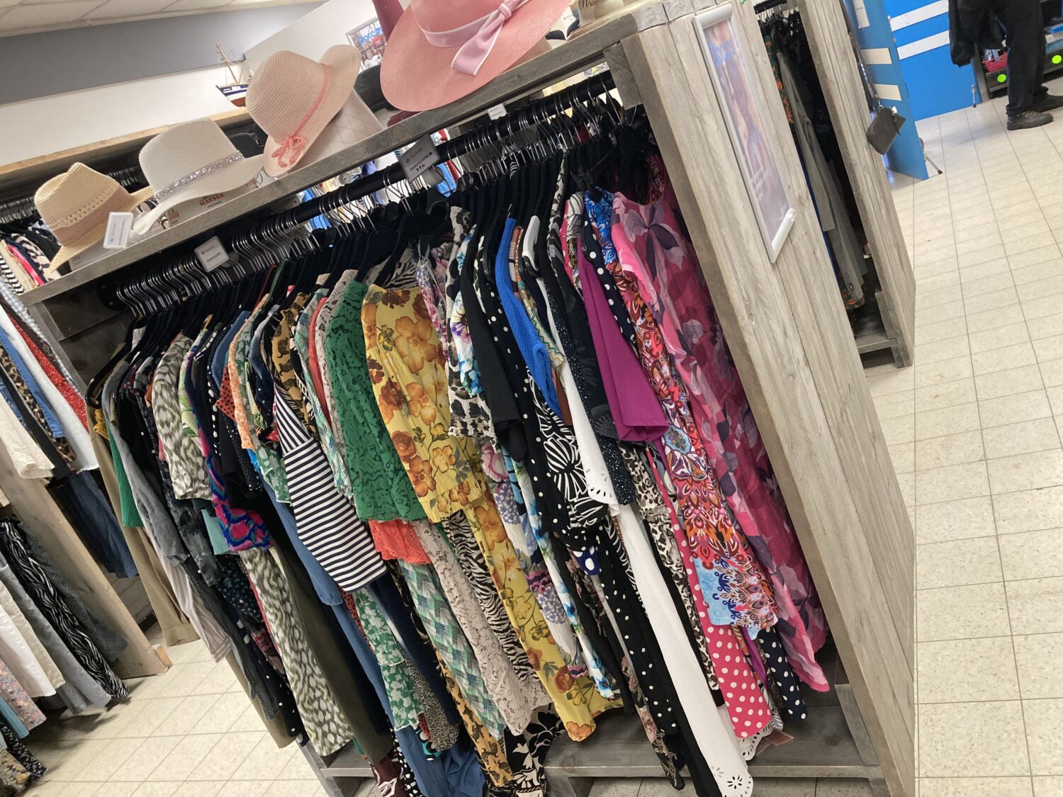Een overzicht van kleurrijke zomeroutfits en hoeden in de winkel, perfect voor de warme dagen.