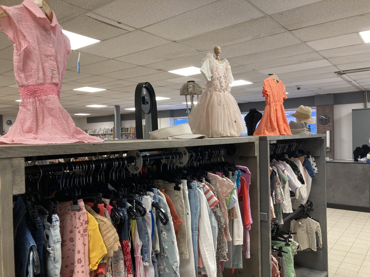 Een overzicht van kinderkleding en poppenmode in een winkel, met diverse outfits en accessoires voor kinderen en poppen.