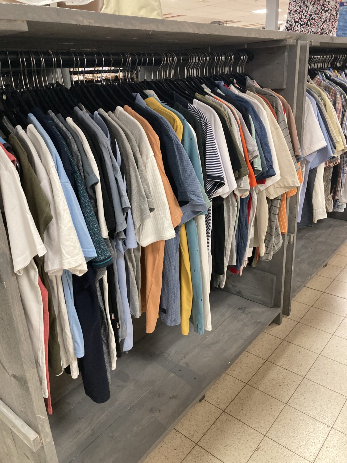 Een overzicht van verschillende T-shirts en shirts in een kledingwinkel, netjes opgehangen aan een kledingrek, klaar voor verkoop.