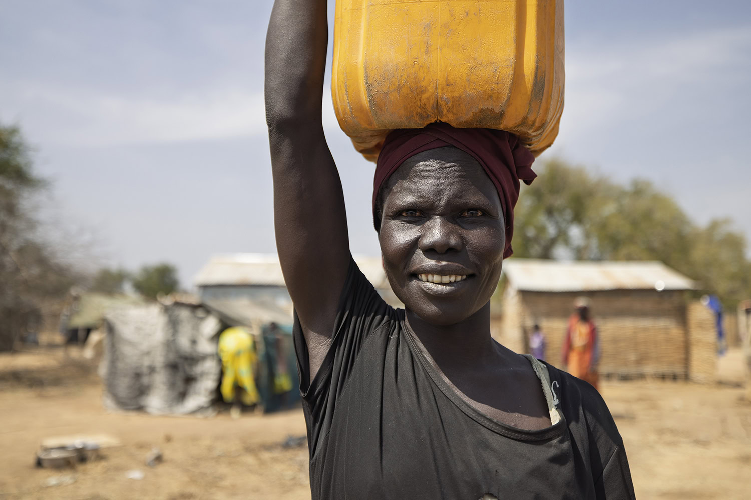 Een vrouw in Kenia draagt een watercontainer op haar hoofd, terwijl ze door een dorre omgeving loopt, wat de uitdaging van het verkrijgen van schoon water benadrukt.