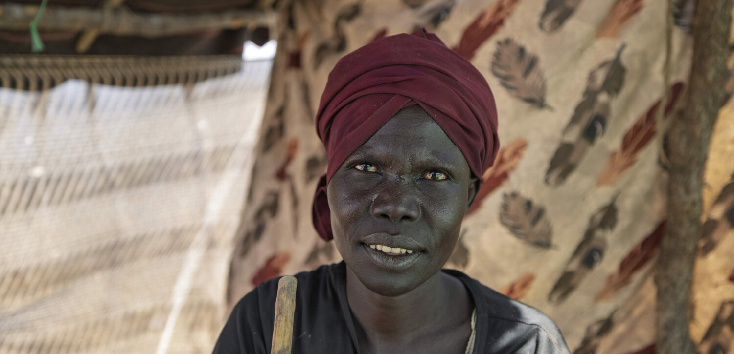 Een vrouw uit Kenia die hulp ontvangt van de voedselbank, met een achtergrond van een tent en een houten hek.