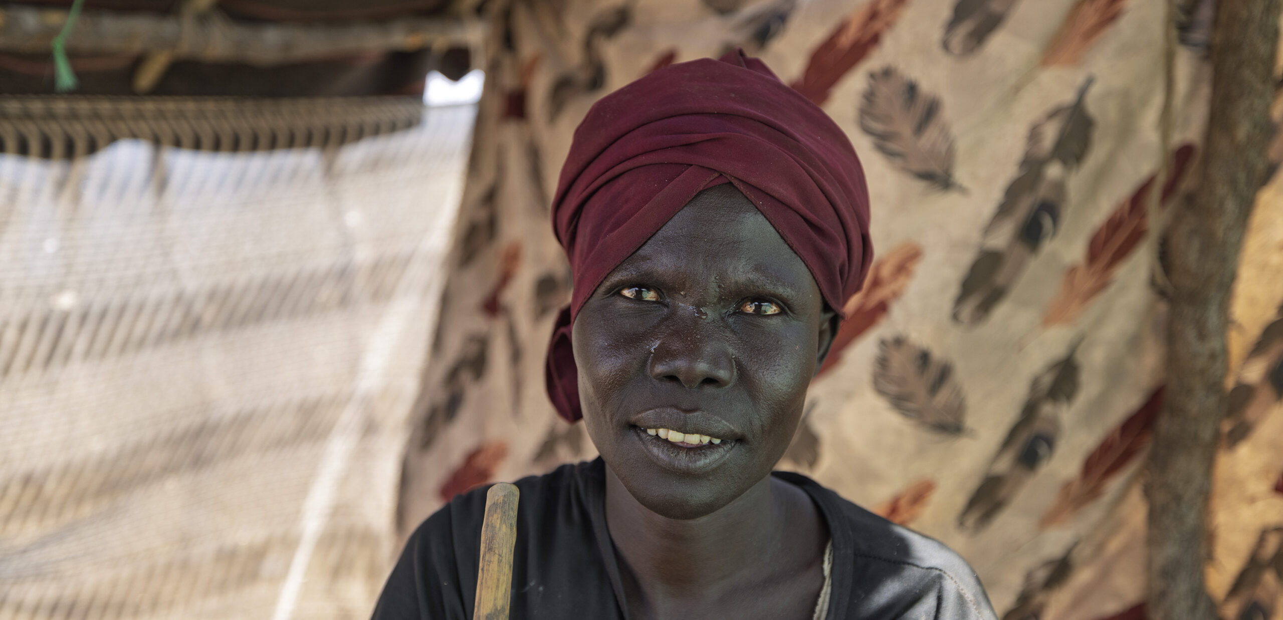 Een vrouw uit Kenia die hulp ontvangt van de voedselbank, met een achtergrond van een tent en een houten hek.