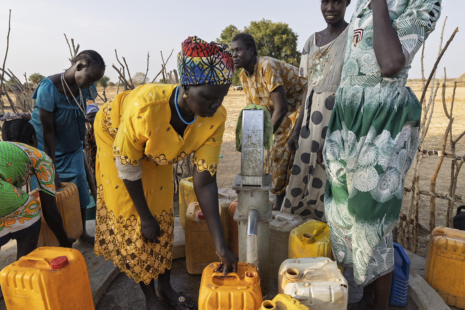 Nyanut en haar kinderen vullen jerrycans met schoon drinkwater bij een waterpunt in een droge omgeving, een illustratie van de impact van waterprojecten van Dorcas.