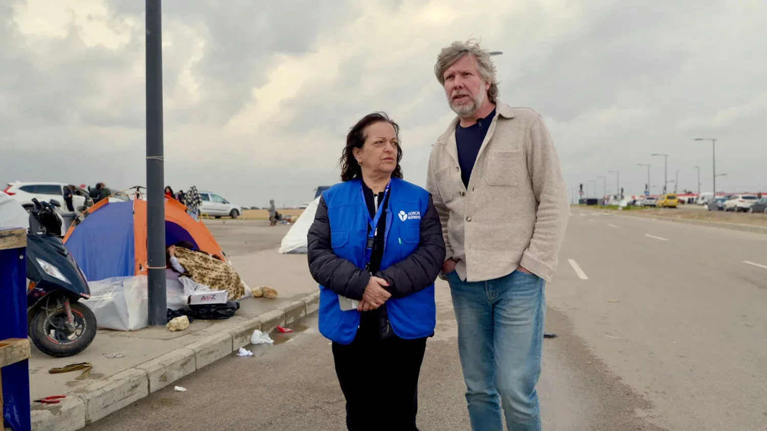 Een hulpverlener en een vrijwilliger staan samen op een parkeerplaats in Libanon, waar vluchtelingen worden geholpen door EO Metterdaad in de context van de noodhulpactie.