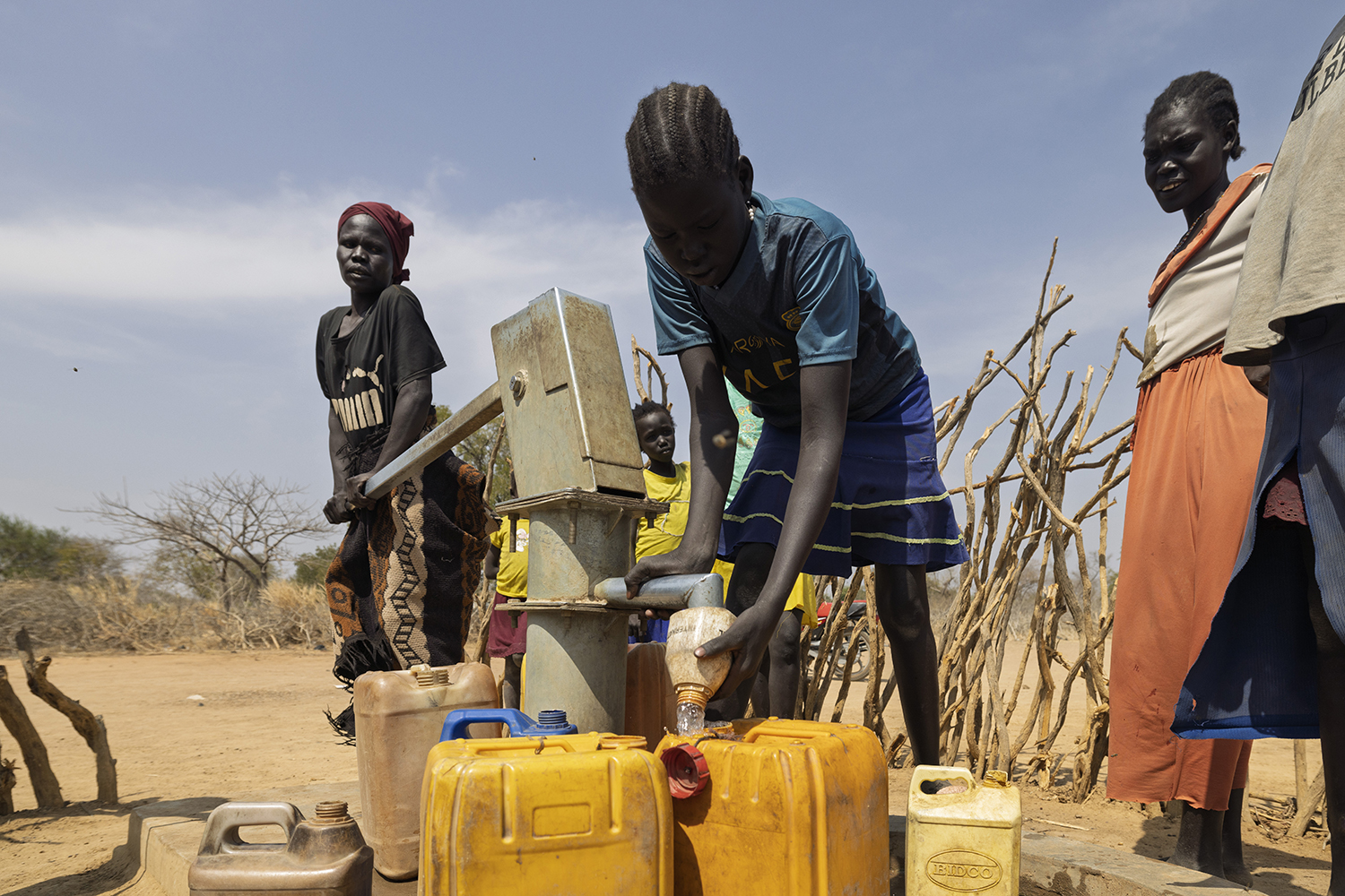 Kinderen in een dorpsomgeving vullen jerrycans met water bij een handpomp, illustrerend de uitdaging van water verkrijgen voor gemeenschappen in droge gebieden.