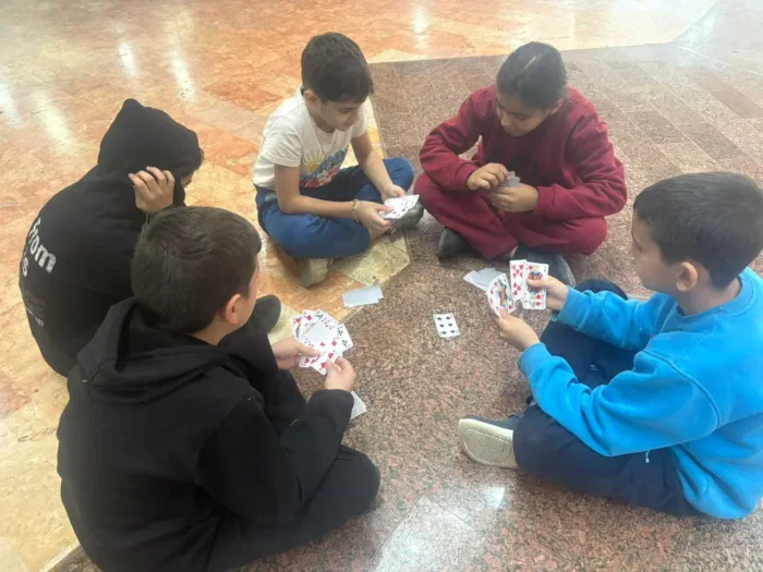 Vijf kinderen zitten op de vloer en spelen samen kaartspellen, ontspannen en plezier hebbend.