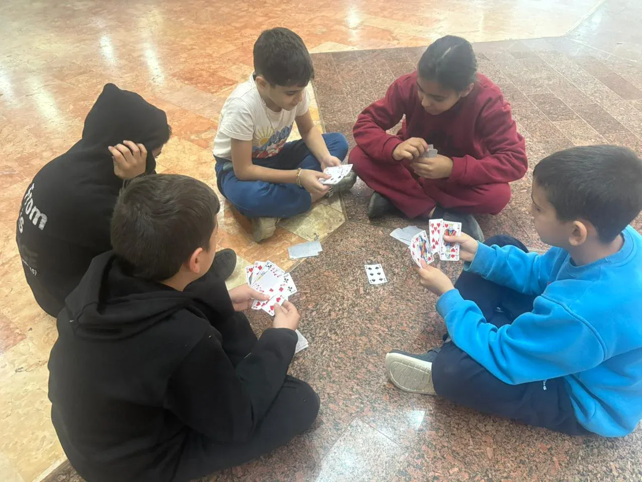 Vijf kinderen zitten op de vloer en spelen samen kaartspellen, ontspannen en plezier hebbend.