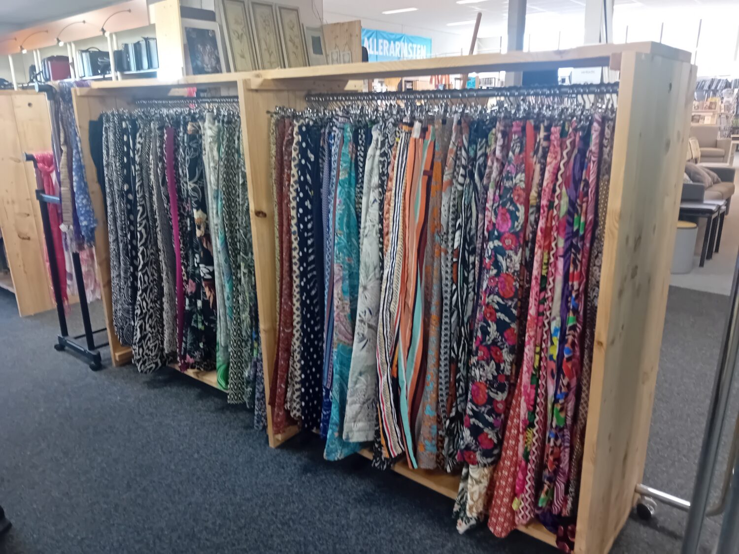 Diverse kleurrijke stoffen en textiel hangen aan kledingrekken in een winkel, klaar voor verkoop of gebruik, met een overzichtelijke presentatie in een winkelomgeving.