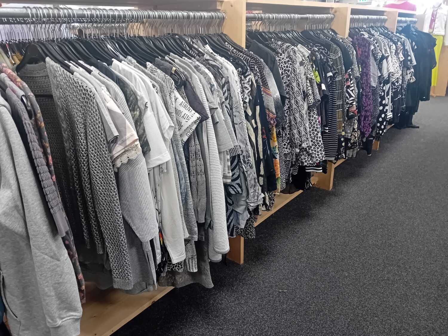 Een overzicht van verschillende dameskleding, zoals blouses, jurken en jassen, uitgestald op een kledingrek in een winkel, geschikt voor tweedehands of duurzame mode.